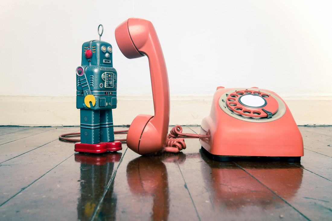A small toy robot is using an old rotary telephone to talk to someone.