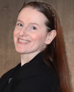 Shari Berg of The Write Reflection is a white woman with long reddish brown hair. She's wearing a black business suit with a bejeweled headband. 