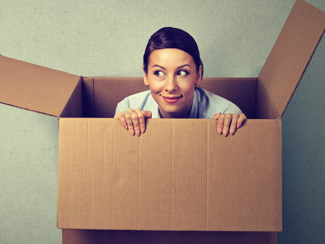 A woman peeks out from inside a cardboard box.