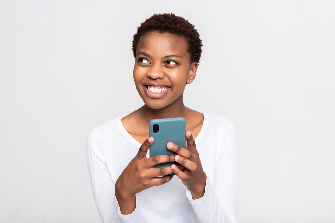 A smiling Black woman uses her mobile phone to conduct business on the Internet. 