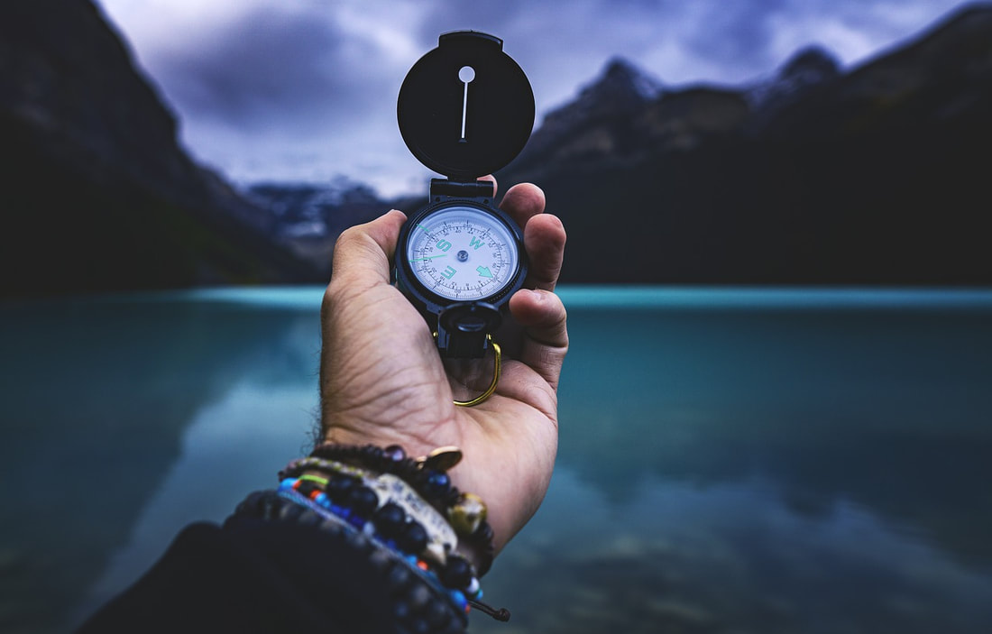 Photo of a man holding out a compass with a lake and mountains in the distance.