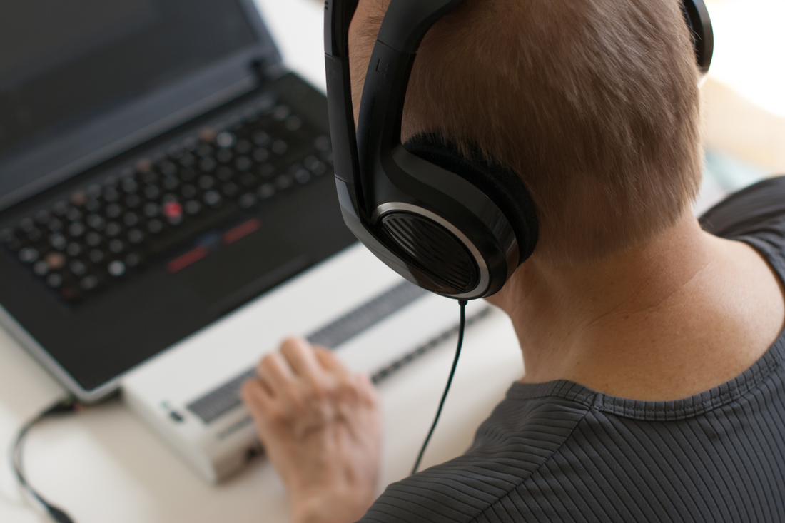 A man wearing noise-canceling headphones uses a screen reader to interpret digital content on his laptop. 