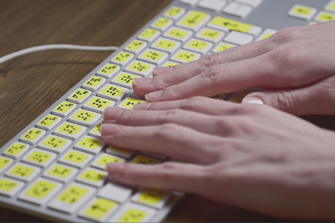 A woman's hands rest on a keyboard adapted for visually impaired users to access digital content. 