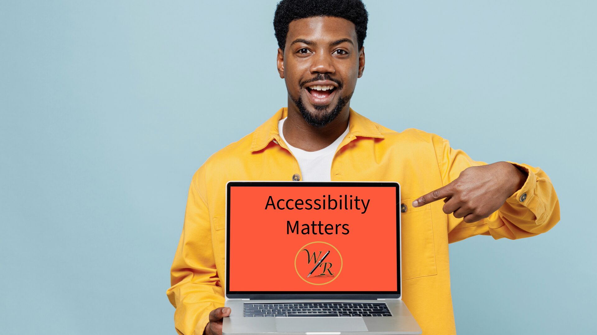 A Black man wearig a yellow shirt and smiling points to a laptop computer screen that says "Accessibility Matters"