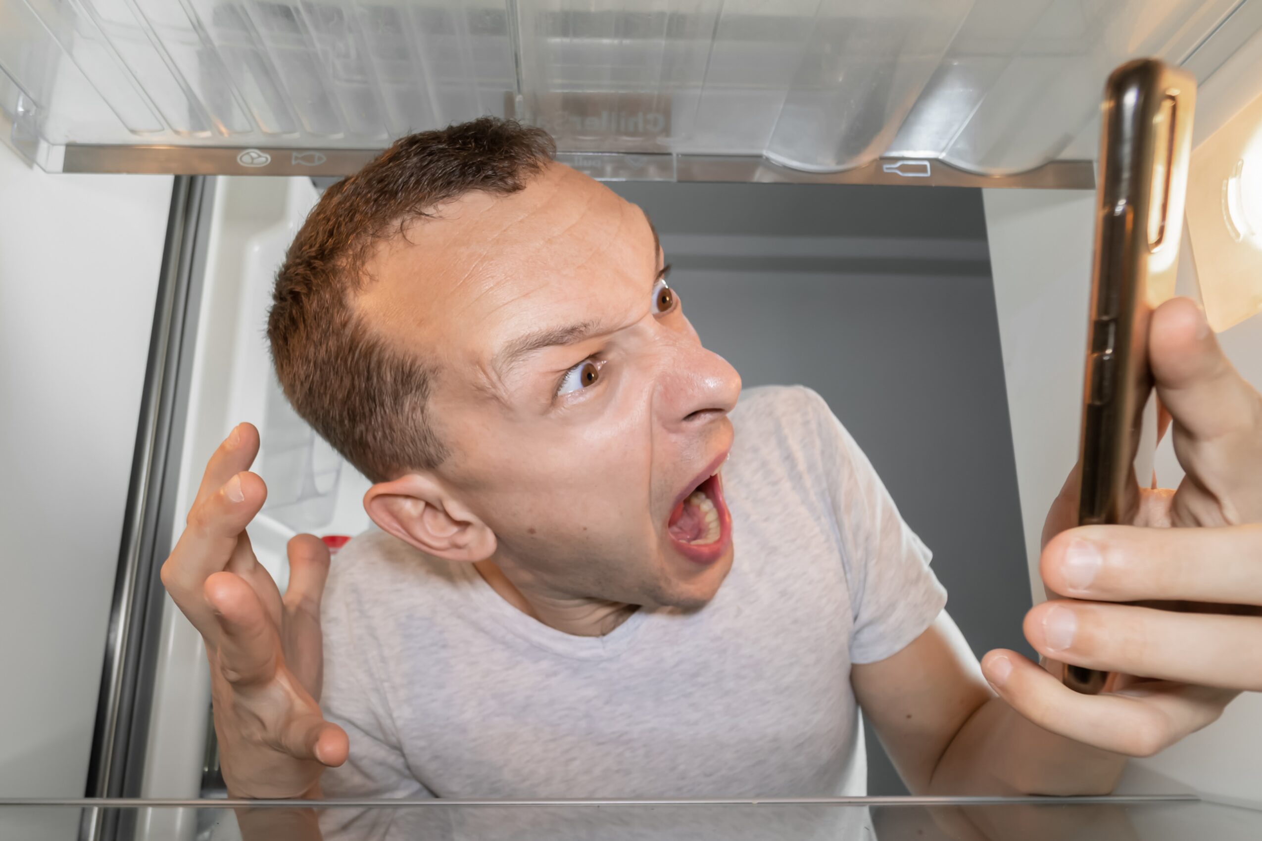 A man holds a cell phone and screams into it.