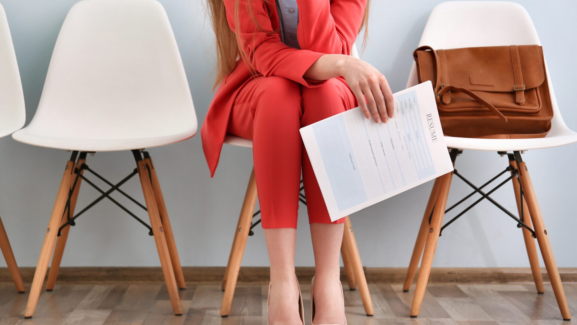 A woman wearing a pink business suit holds a resume in her hand as she sits and waits for her job interview.