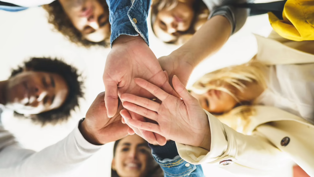 A group of small business owners form hands into a pile in support of one another. 