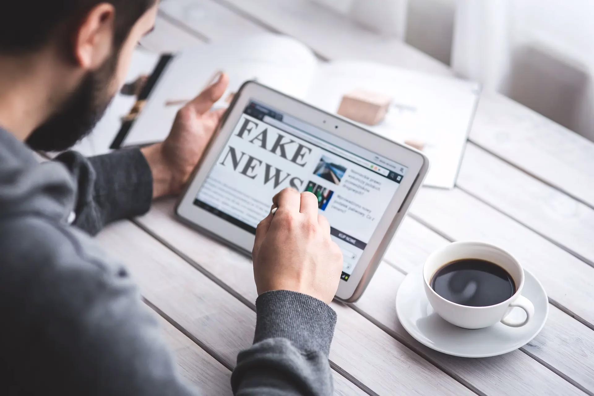 A man reads a fake news article on his mobile device while drinking some coffee.